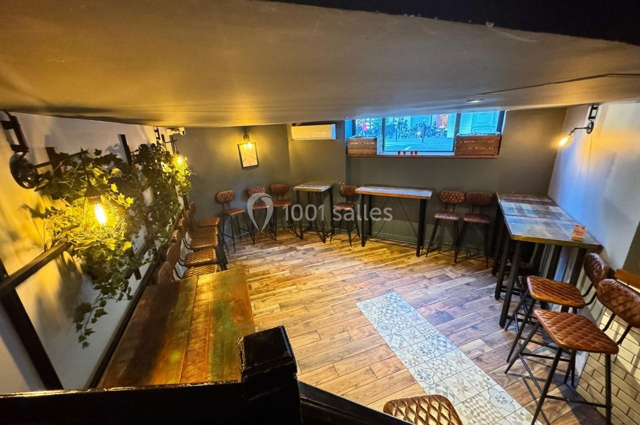 Salle lumineuse avec tables hautes, tabourets en cuir, sol en bois et décorations murales végétales.