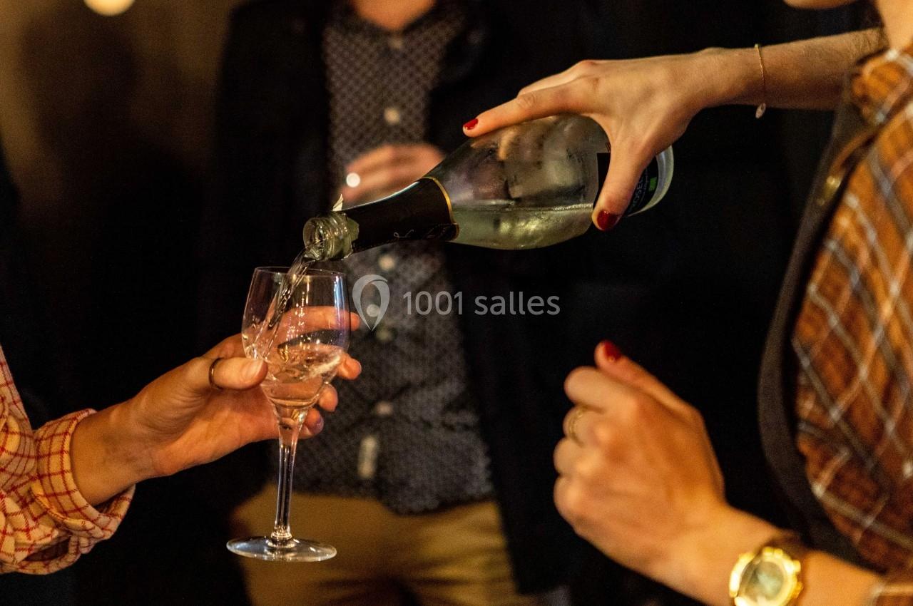 Une personne verse du vin blanc pétillant dans un verre tenu par une autre personne lors d'un rassemblement.