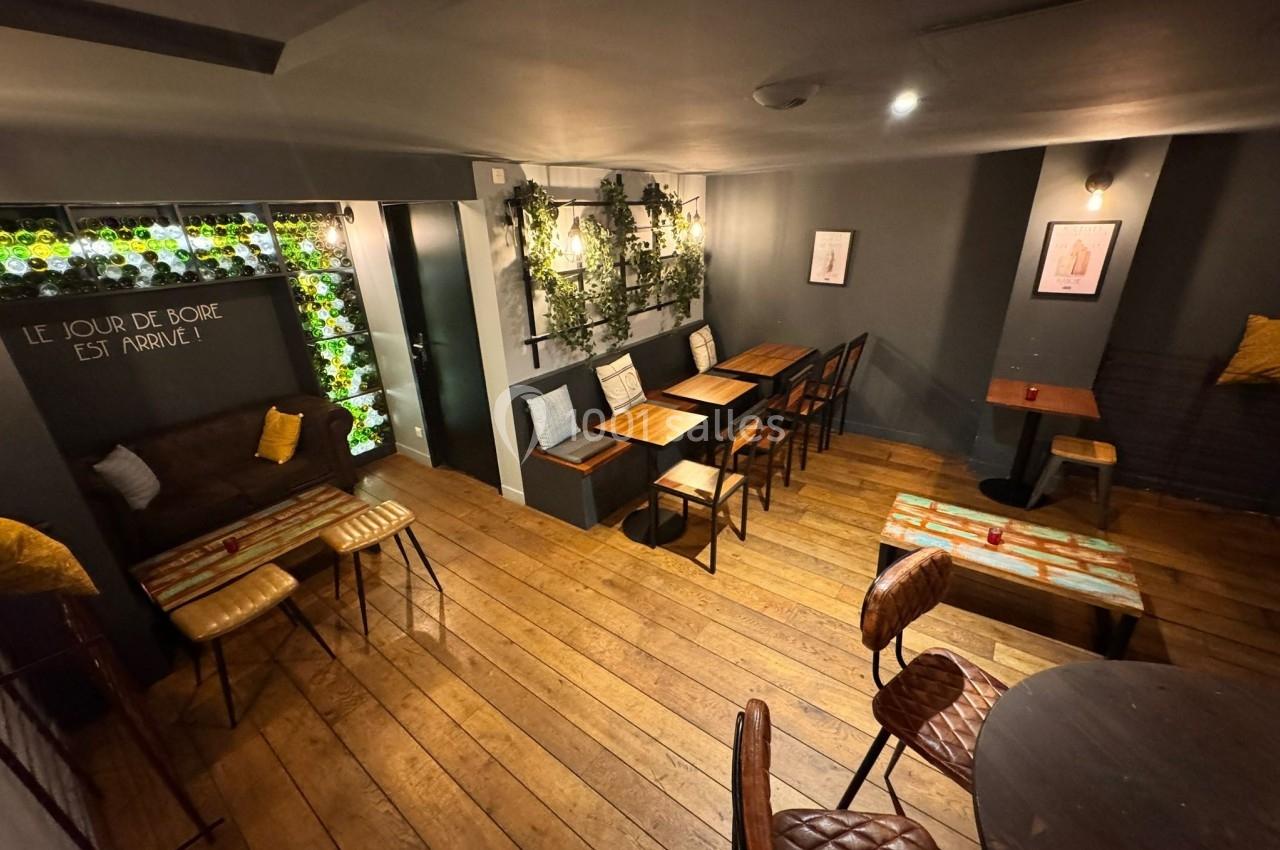 Salle de café cosy avec tables en bois, chaises rembourrées, murs décorés de plantes et éclairage tamisé.