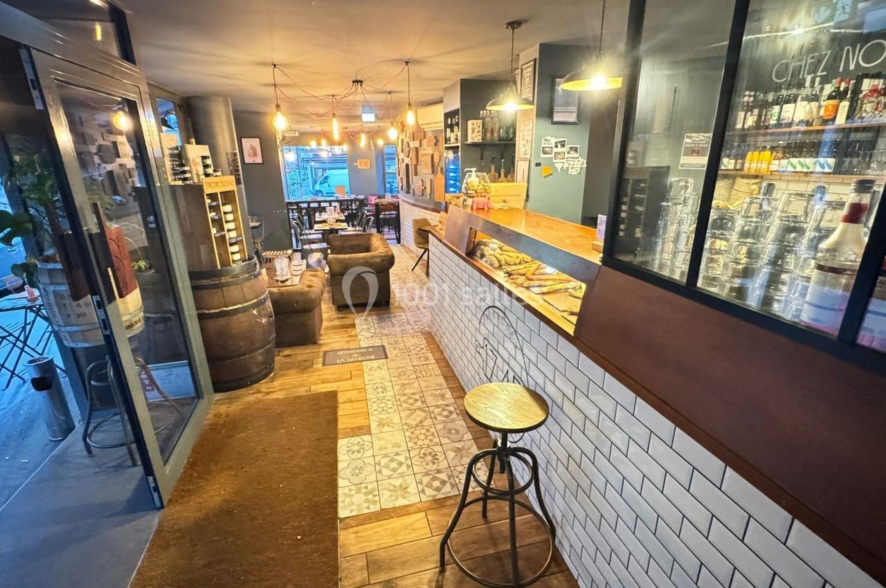 Intérieur d'un café avec comptoir en bois, étagères de boissons, tables et chaises dans une ambiance chaleureuse.