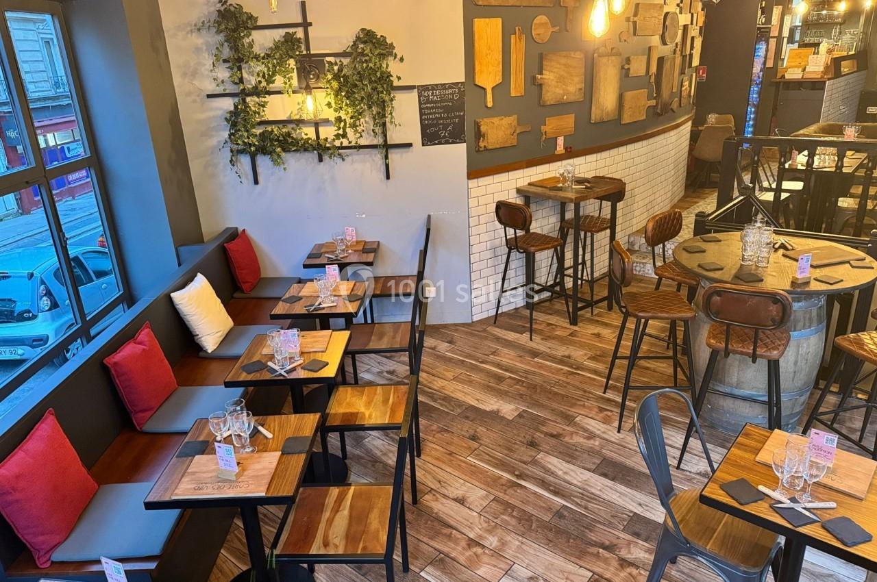 Salle de restaurant chaleureuse avec tables en bois, banquettes colorées, luminaires suspendus et décoration murale.