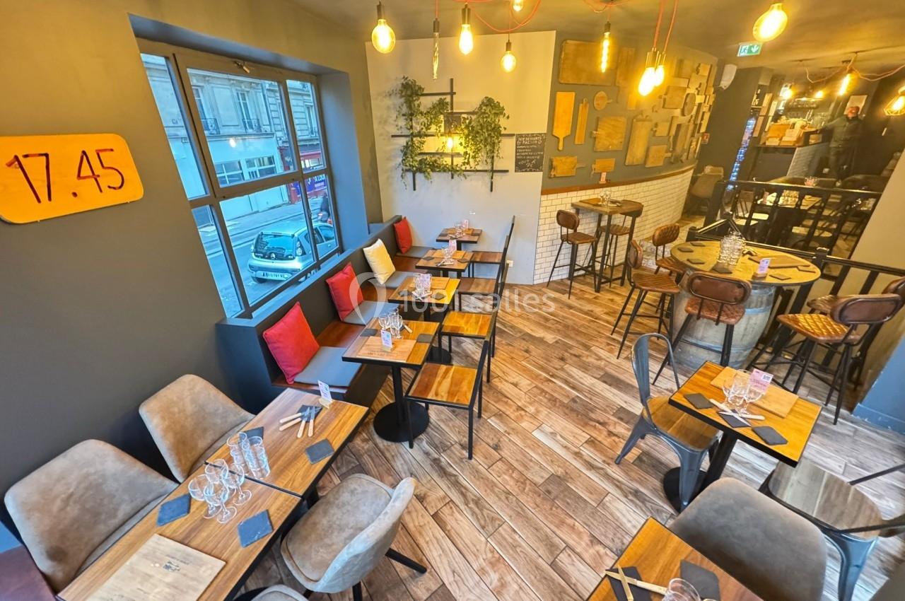 Salle de restaurant lumineuse avec tables en bois, chaises rembourrées, décoration murale et grandes fenêtres.