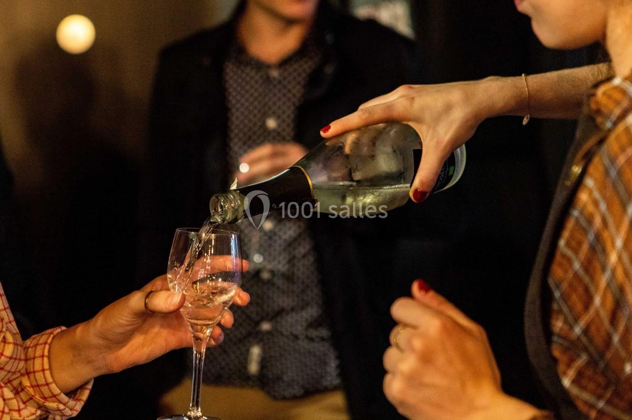 Une personne verse du vin blanc pétillant dans un verre tenu par une autre personne lors d'une soirée conviviale.