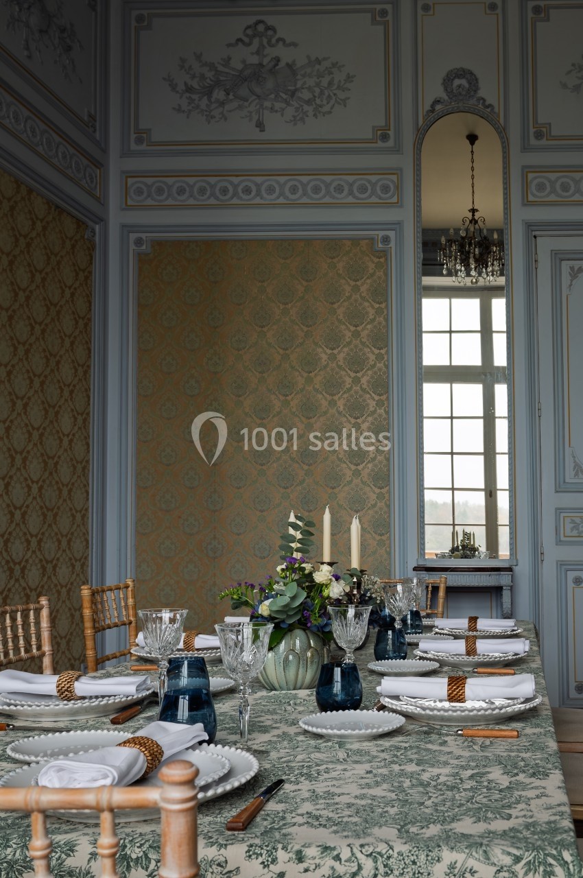 Table élégamment dressée dans une salle ornée de moulures et de motifs, avec des chandeliers et un miroir en arrière-plan.