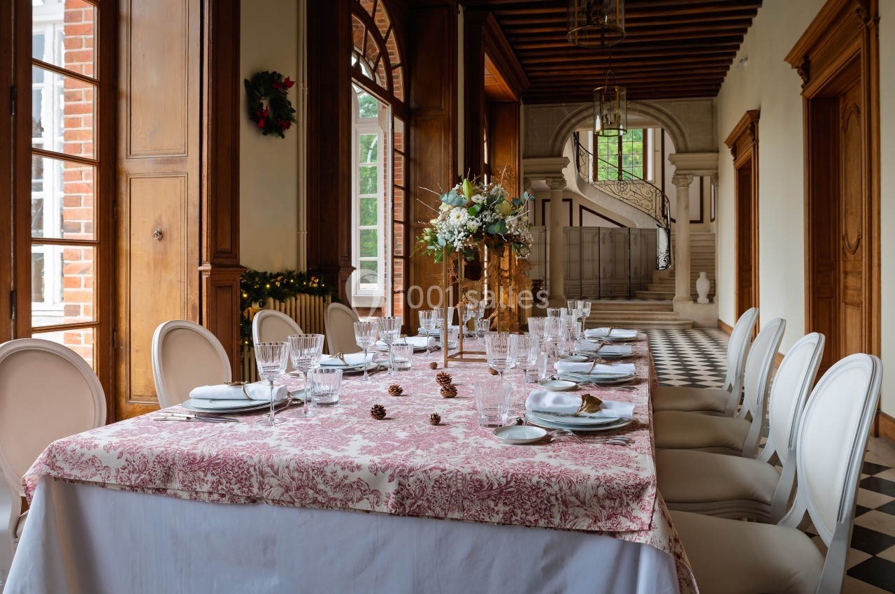 Table élégamment dressée avec nappe à motifs, vaisselle raffinée et centre de table floral, dans une salle lumineuse.