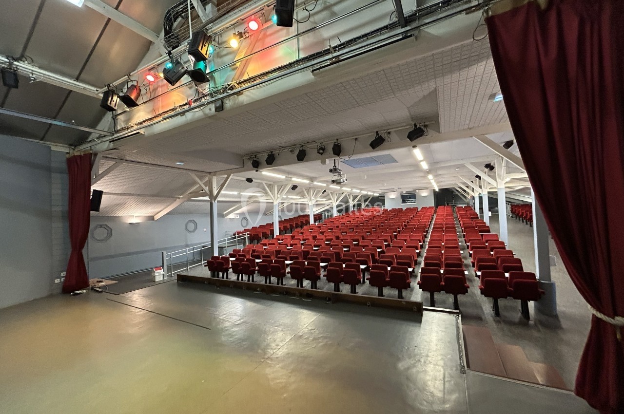 Vue depuis une scène sur une salle de spectacle avec des rangées de sièges rouges et un éclairage au plafond.