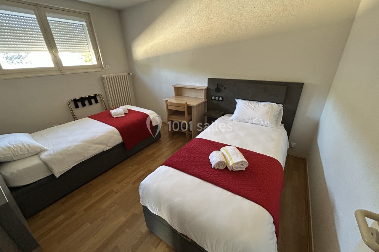 Deux lits simples avec couettes blanches et plaids rouges dans une chambre lumineuse au sol en parquet.