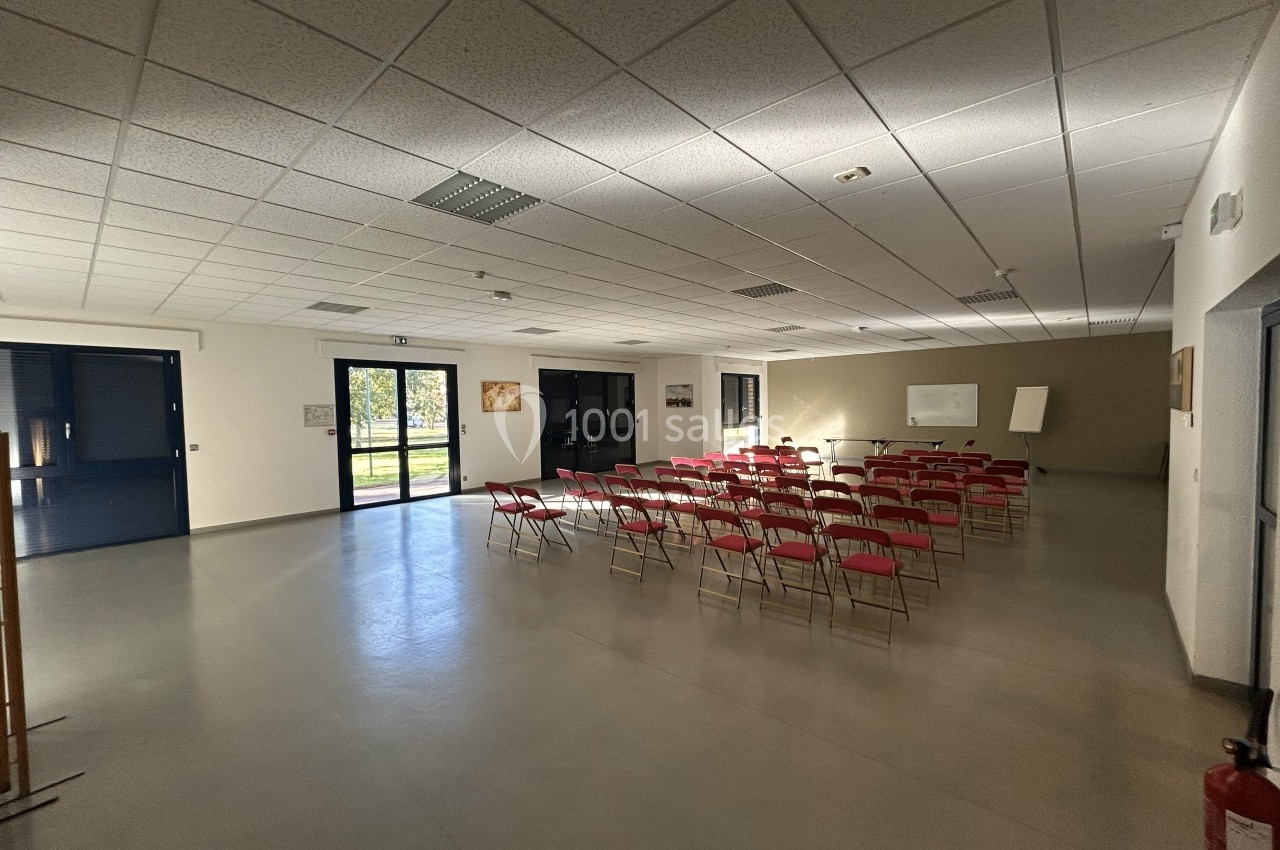 Salle lumineuse avec des chaises rouges alignées face à un tableau blanc, portes vitrées ouvertes sur l'extérieur.