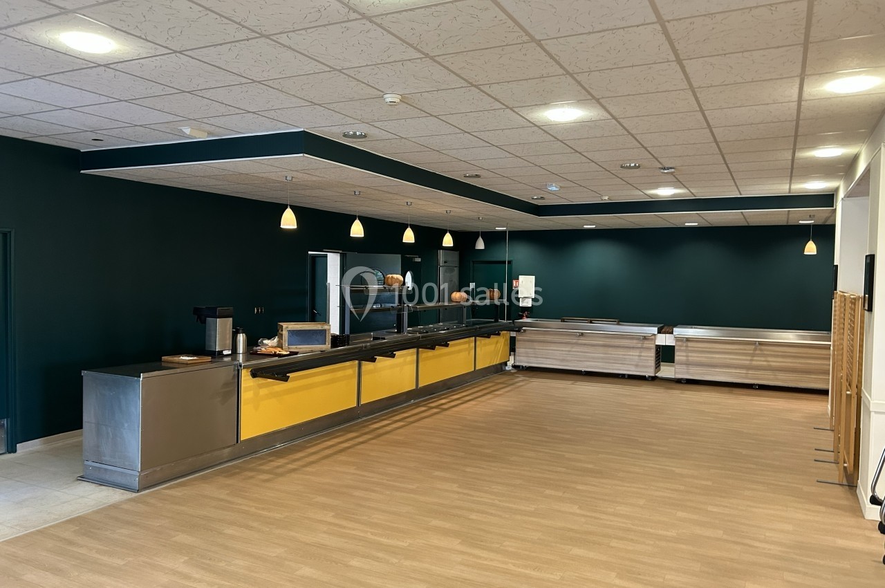 Salle de restauration avec comptoirs en inox et jaune, éclairage suspendu et sol en parquet clair.