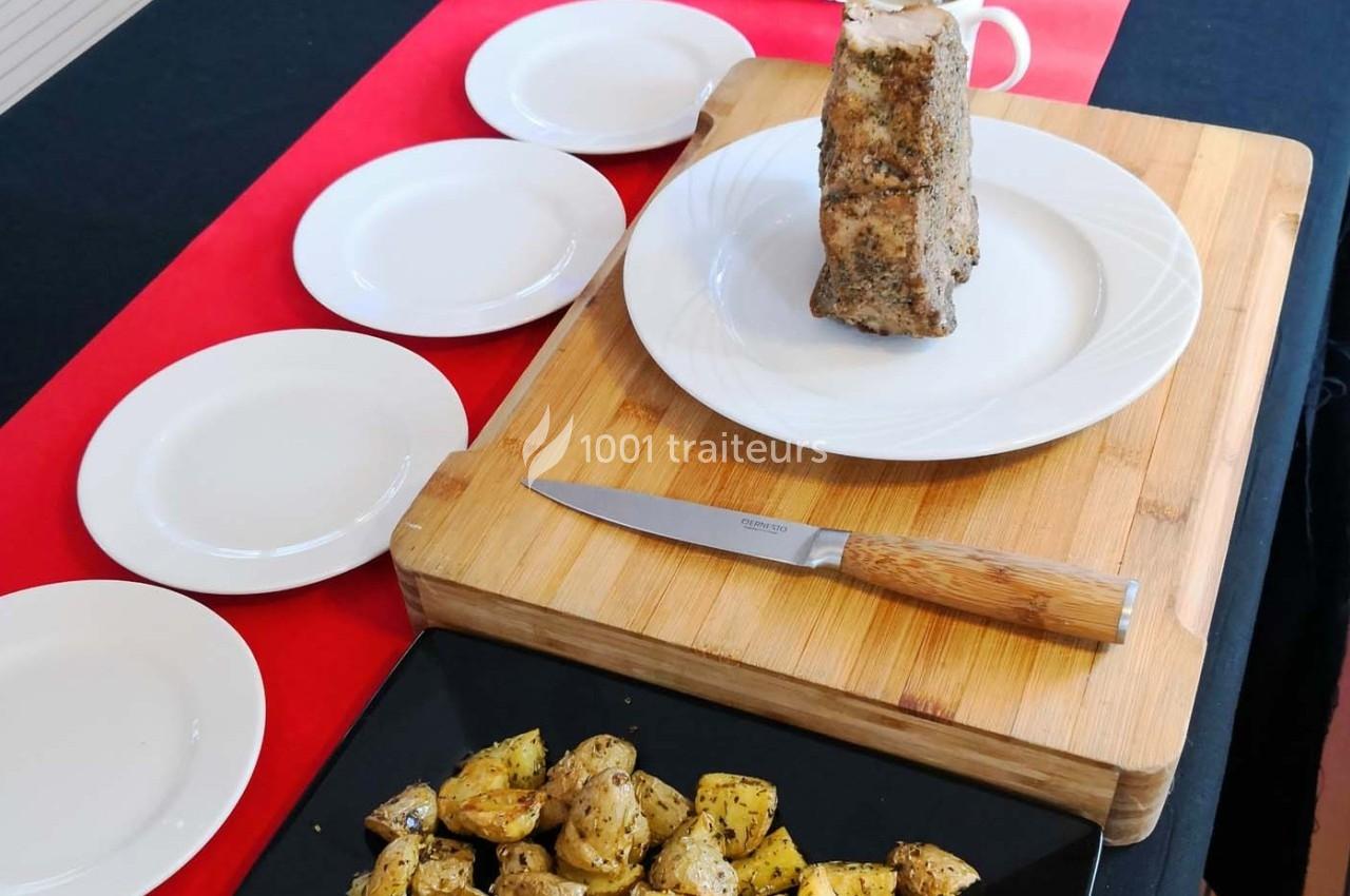 Un rôti assaisonné sur une assiette blanche, un couteau en bois et des pommes de terre rôties sur un plat noir.