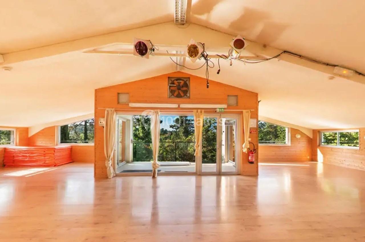 Salle lumineuse avec parquet, grandes baies vitrées donnant sur un paysage verdoyant, et matériel rangé sur les côtés.
