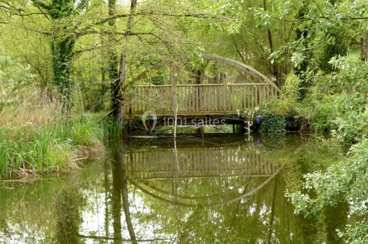 Pont en bois courbé traversant un étang calme entouré de végétation verdoyante.