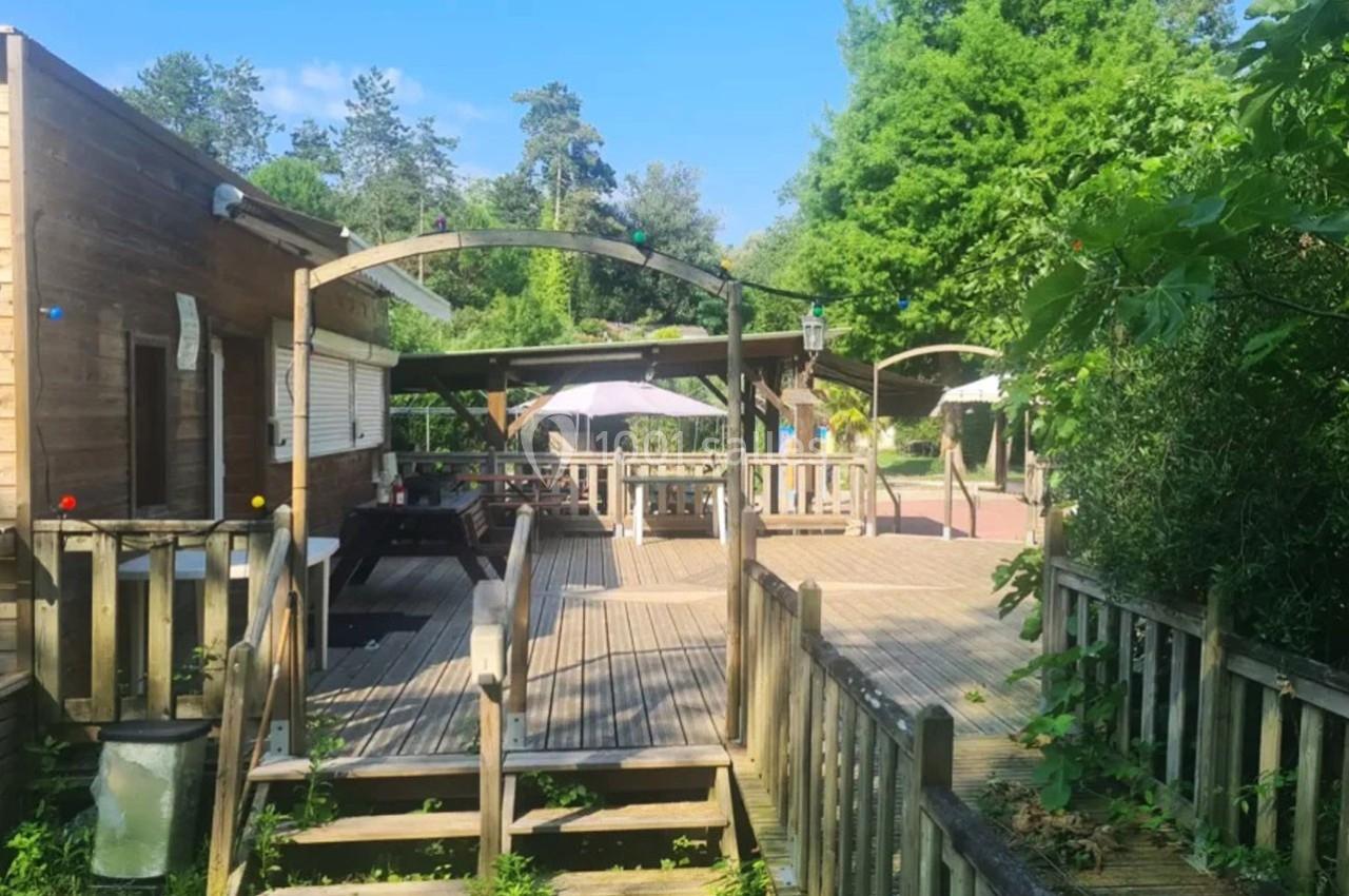 Terrasse en bois avec tables, parasols et pergolas, entourée de végétation sous un ciel ensoleillé.