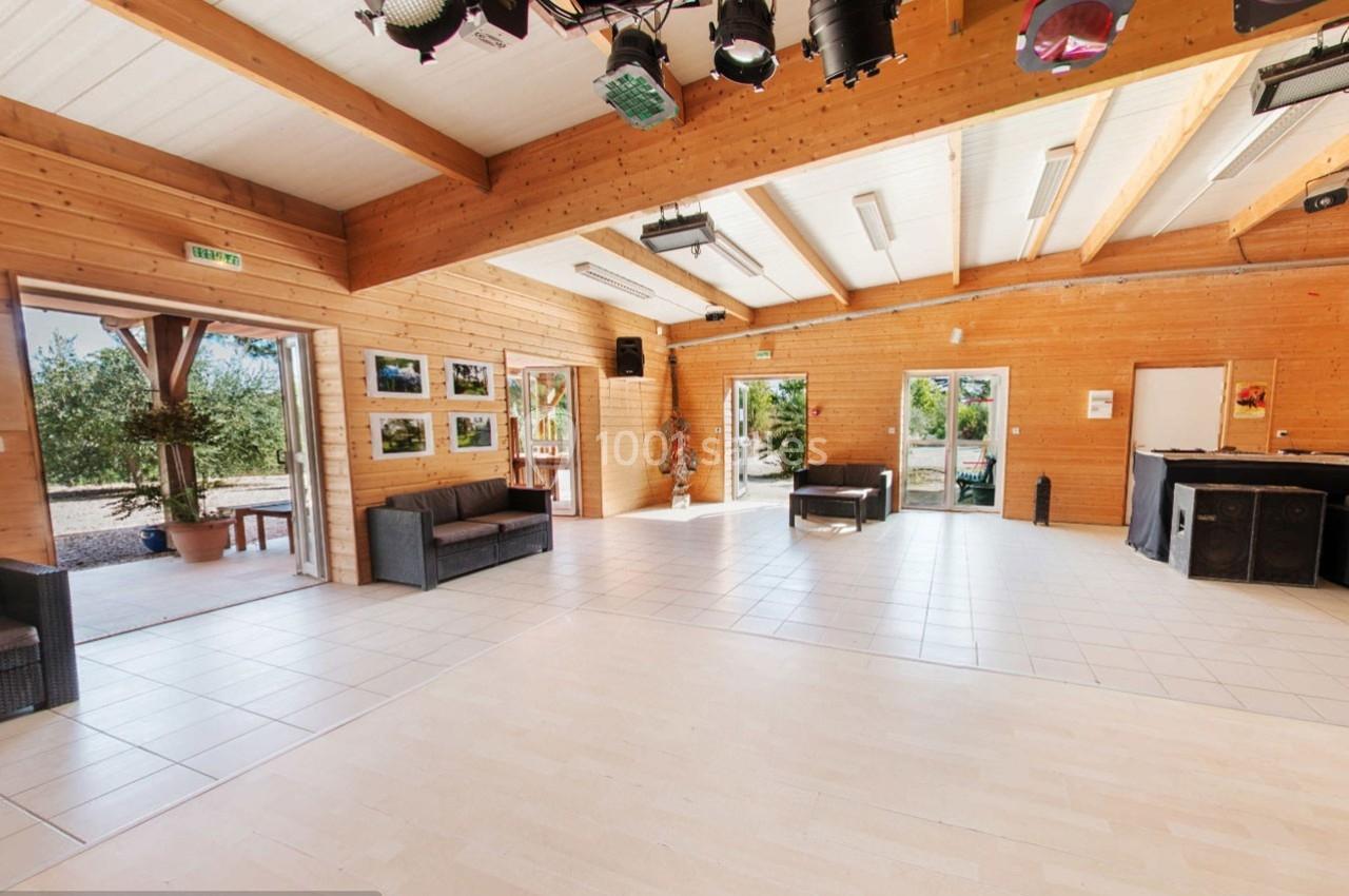 Salle lumineuse avec murs en bois, grandes fenêtres, canapés, et vue sur un extérieur arboré.