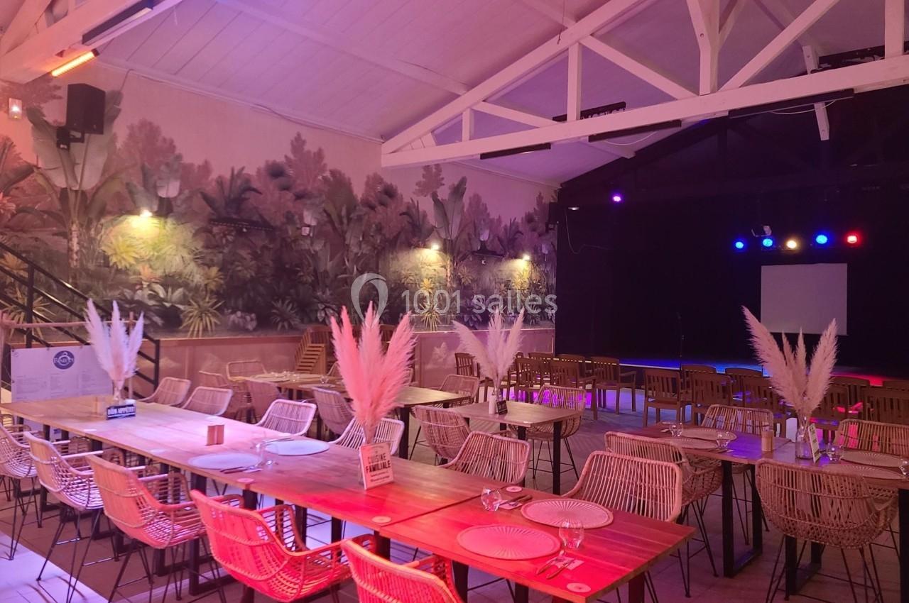Salle de réception décorée avec des tables en bois, chaises en rotin, plantes murales et éclairage coloré.