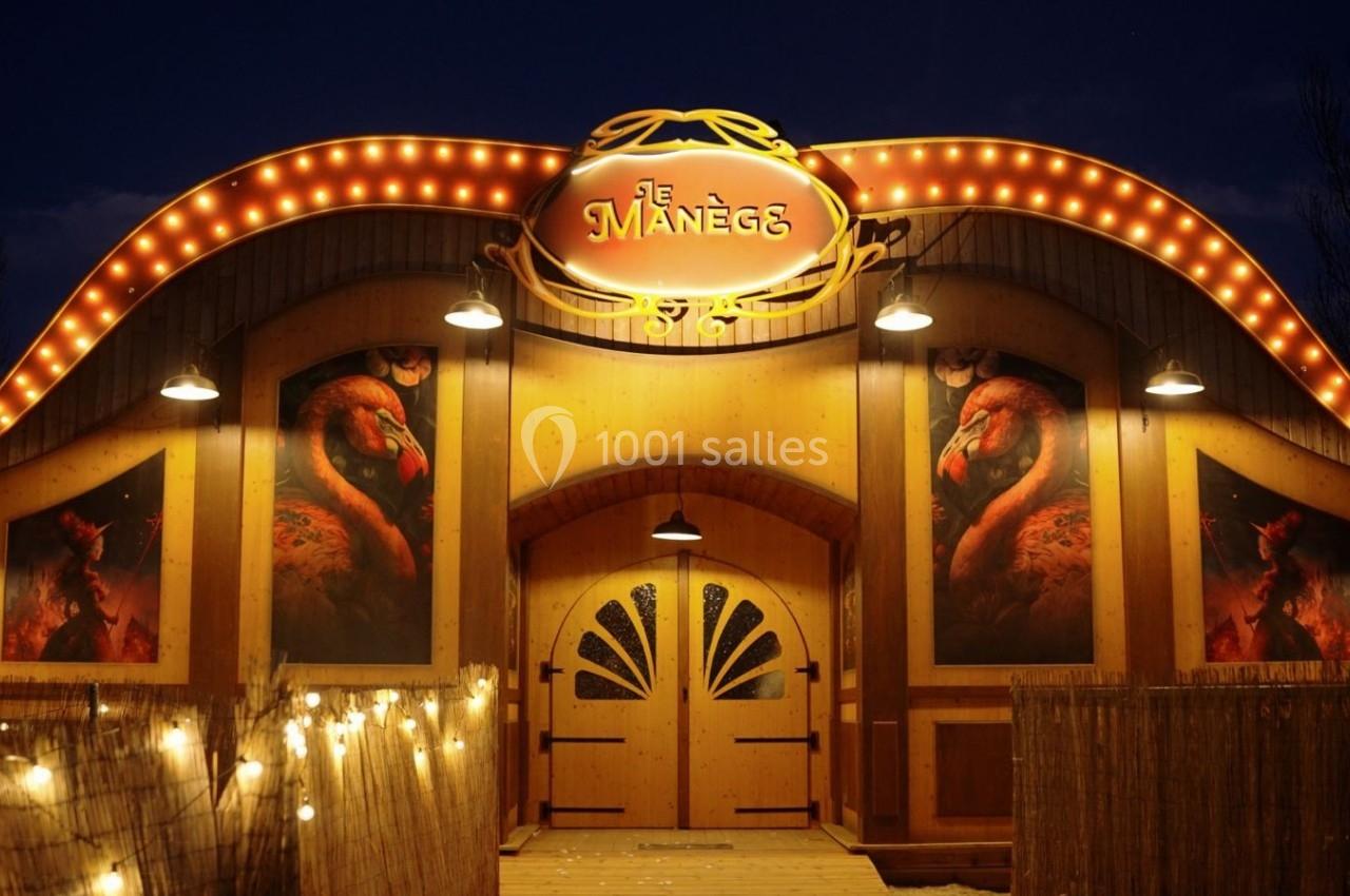 Façade illuminée d'un bâtiment en bois avec une enseigne ’Le Manège’ et des images de flamants roses.