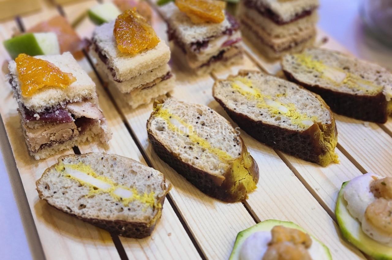 Plateau en bois avec des amuse-bouches variés, incluant des toasts, des tranches de pain garnies et des bouchées sur…