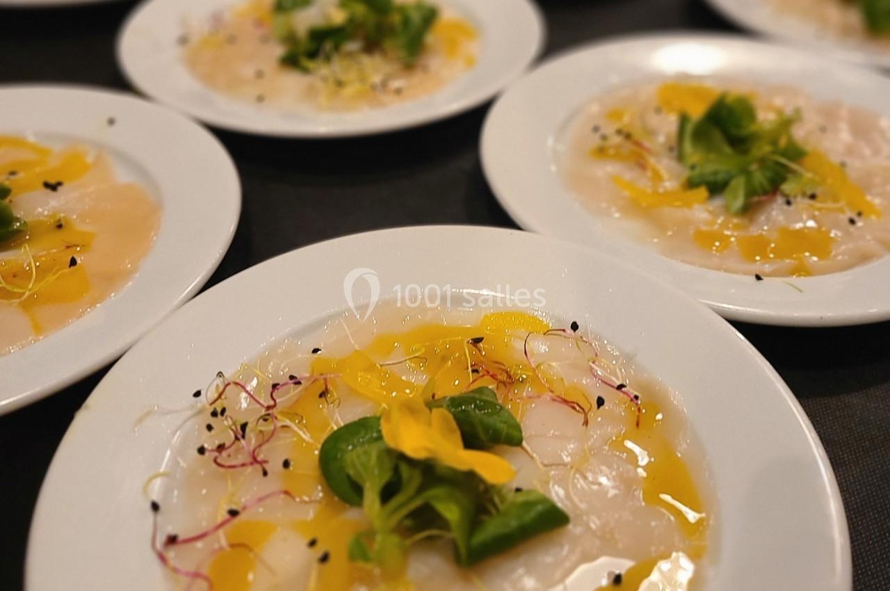Assiettes de carpaccio de poisson garnies de micro-pousses, fleurs comestibles et filet d'huile.