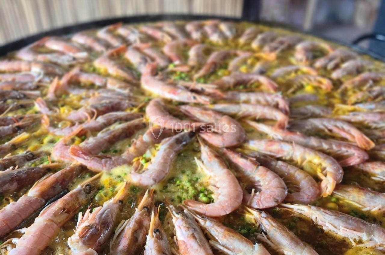 Grande poêle de paella garnie de crevettes disposées en cercle sur un fond de riz safrané.