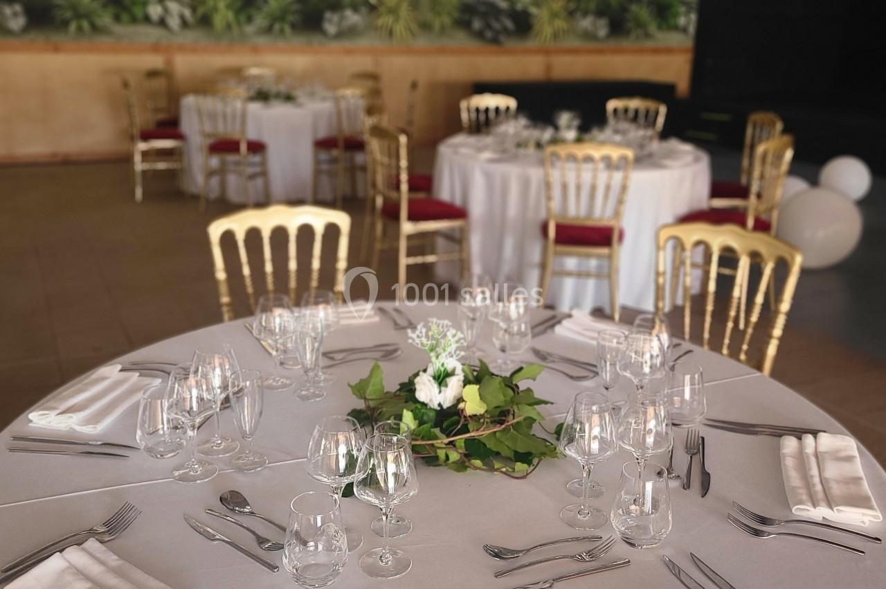 Table ronde dressée avec nappes blanches, couverts élégants et centre de table floral, dans une salle décorée de fresques…