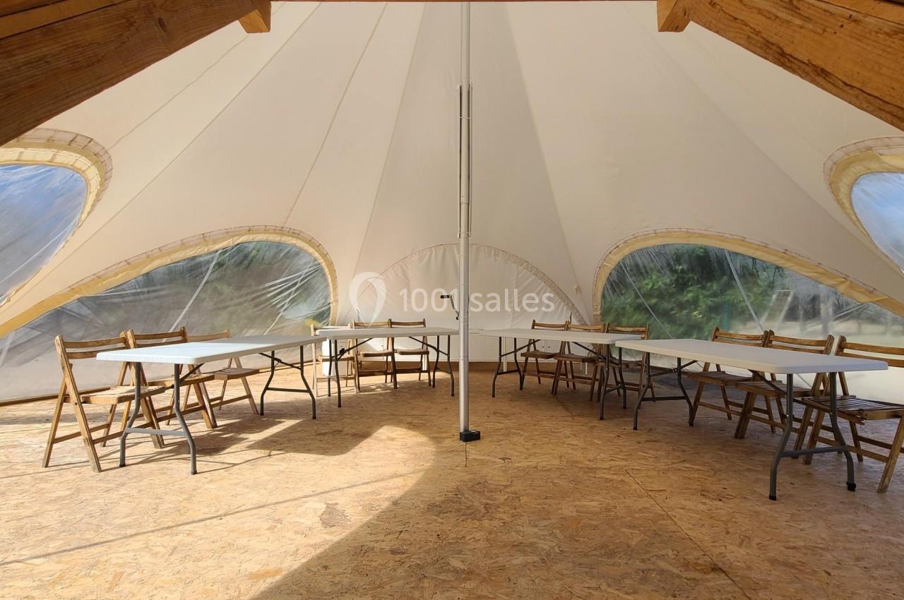 Intérieur d'une tente avec des tables pliantes et des chaises en bois disposées sur un sol en panneaux de bois.