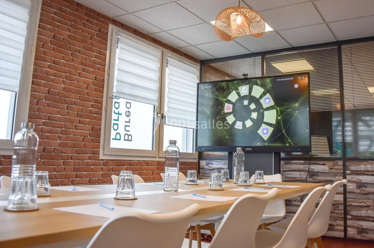 Salle de réunion lumineuse avec table en bois, chaises blanches, bouteilles d'eau, verres et écran affichant un graphique.