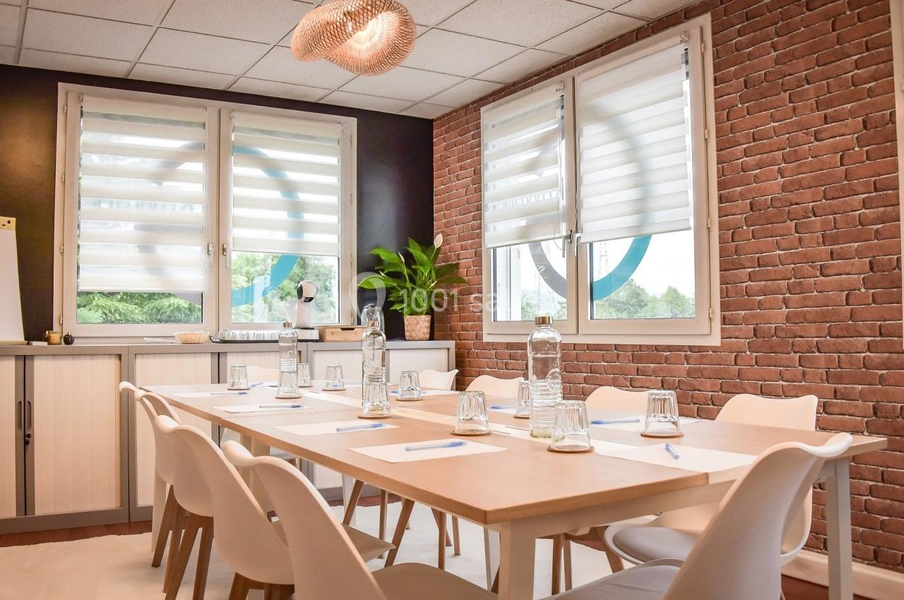Salle de réunion lumineuse avec table en bois, chaises blanches, bouteilles d'eau, verres et plante en arrière-plan.