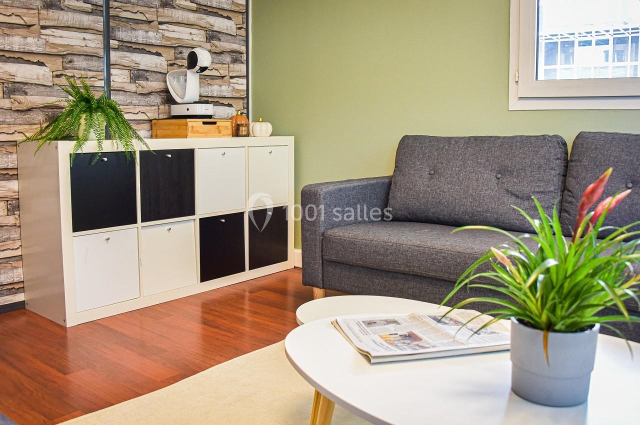 Salon avec canapé gris, table basse blanche, étagère à casiers, plantes vertes et mur à motif bois.