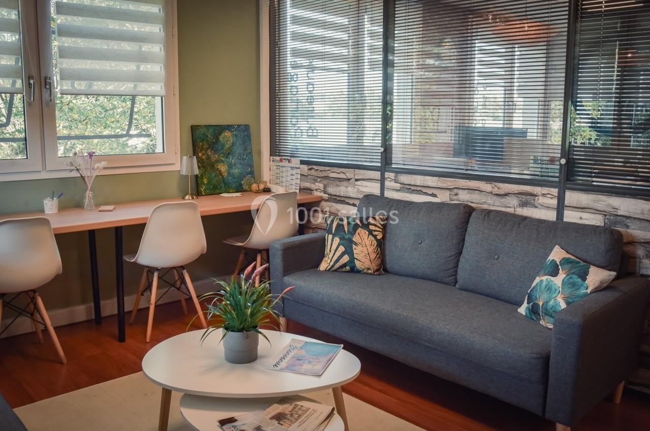 Espace intérieur lumineux avec canapé gris, table basse, chaises blanches et bureau près d'une fenêtre.