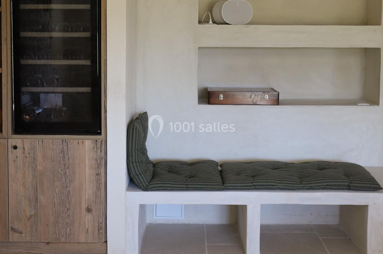 Banc en béton avec coussin rayé vert, étagères intégrées contenant une boîte en bois et une enceinte, à côté d'une cave à…