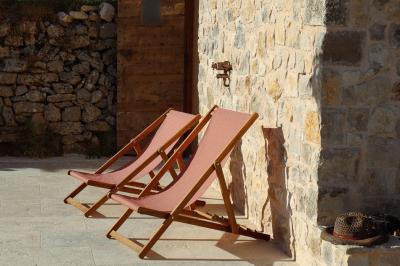 Deux chaises longues en bois et tissu rouge posées sur une terrasse en pierre, adossées à un mur en pierre.