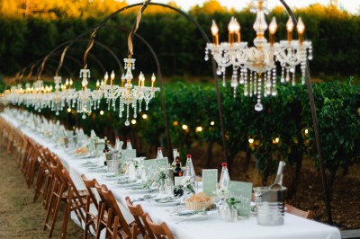Un couple en tenue de mariage marche main dans la main dans un vignoble, la mariée levant un bouquet.