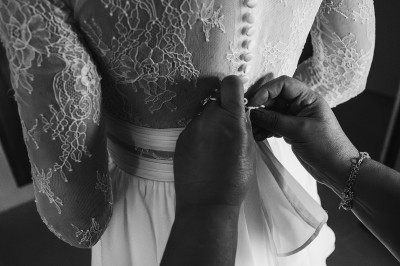 Un couple en tenue de mariage marche main dans la main dans un vignoble, la mariée levant un bouquet.