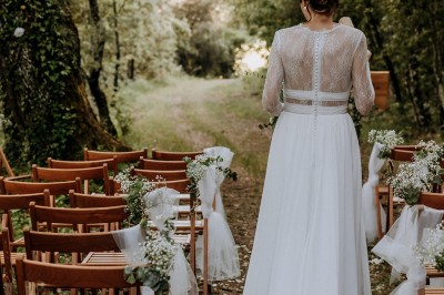 Un couple en tenue de mariage marche main dans la main dans un vignoble, la mariée levant un bouquet.