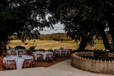Un couple en tenue de mariage marche main dans la main dans un vignoble, la mariée levant un bouquet.