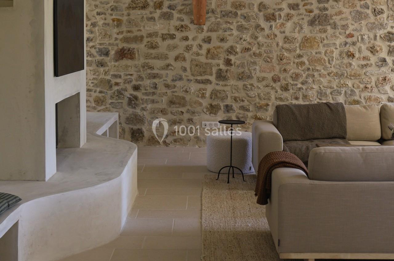 Salon avec murs en pierre apparente, canapé beige, table d'appoint noire et cheminée moderne en béton.