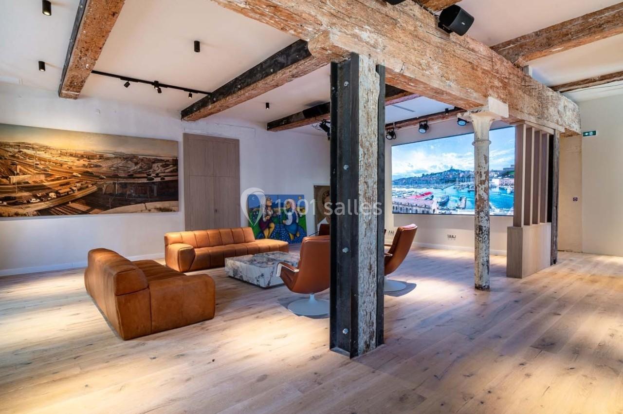 Espace intérieur lumineux avec poutres apparentes, mobilier contemporain et œuvres d'art exposées sur les murs.