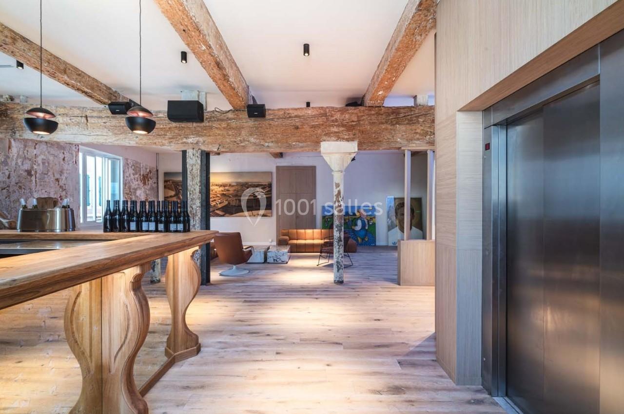 Espace intérieur lumineux avec poutres apparentes, parquet en bois, bar en bois sculpté et ascenseur moderne.
