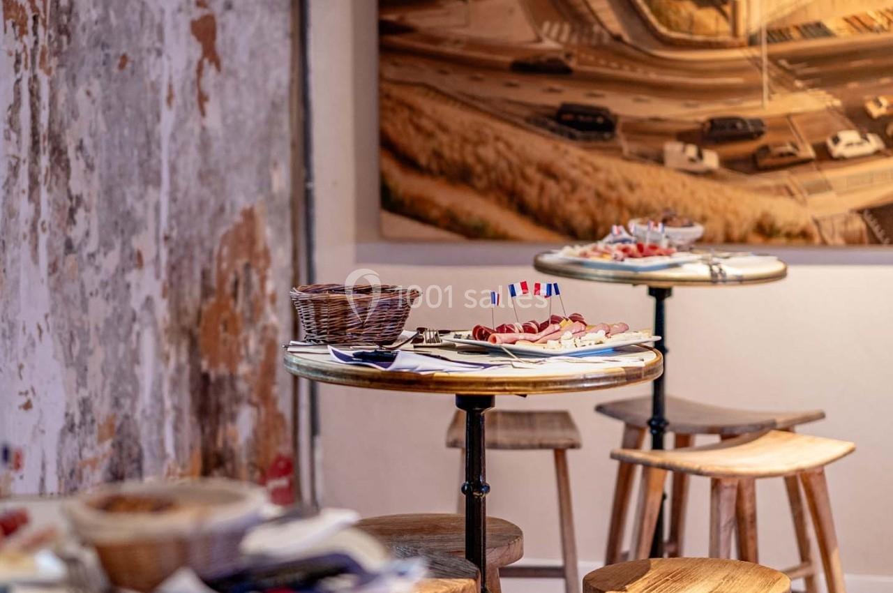 Tables en bois avec assiettes de charcuterie et paniers, dans un décor rustique avec une photo murale en arrière-plan.