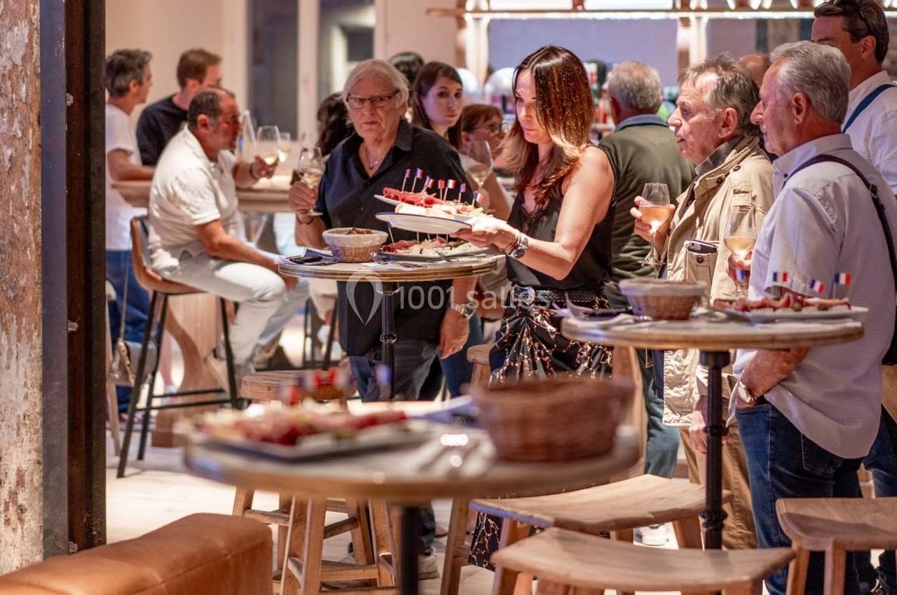 Des personnes discutent et se servent des amuse-bouches dans un espace convivial avec des tables hautes.