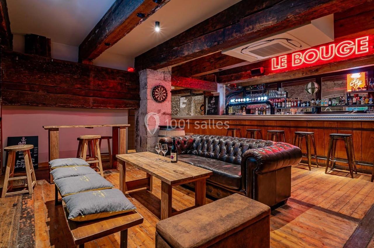 Intérieur d'un bar avec mobilier en bois, canapé en cuir, éclairage chaleureux et enseigne lumineuse rouge.