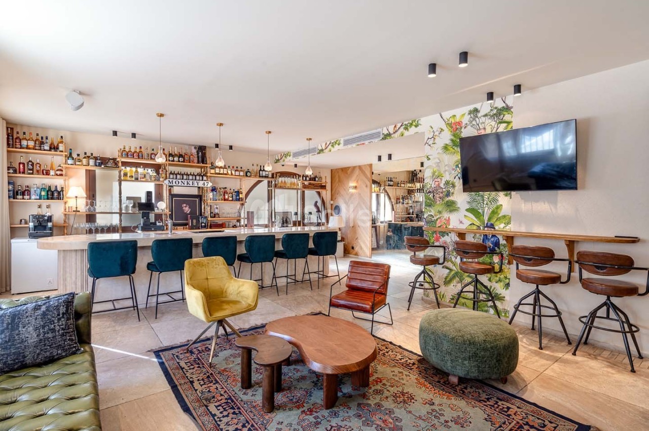 Intérieur d'un bar moderne avec comptoir, tabourets, fauteuils colorés, tables basses et décoration murale florale.