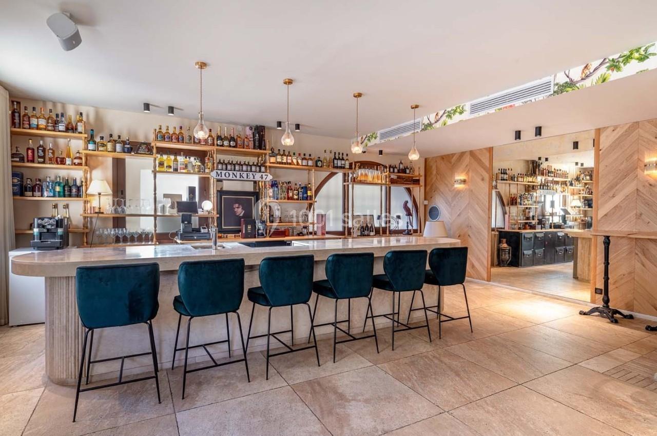 Bar moderne avec comptoir en marbre, tabourets noirs, étagères remplies de bouteilles et éclairage suspendu.