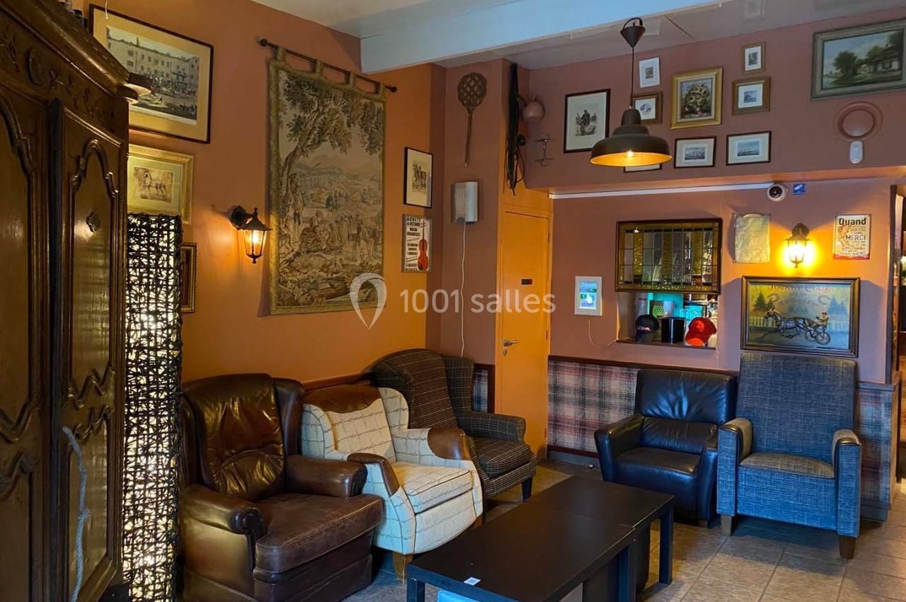 Salon chaleureux avec fauteuils en cuir et tissu, décoré de cadres, tapisseries et objets anciens sur des murs orangés.