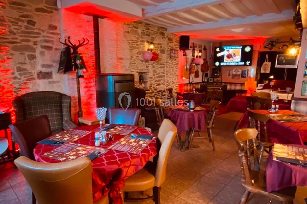 Salle de restaurant chaleureuse avec murs en pierre, éclairage rouge, tables dressées et décorations variées.