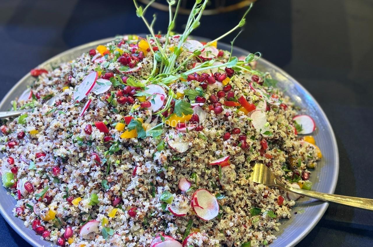 Salade de quinoa garnie de radis, grenade, herbes fraîches et légumes colorés, servie sur une assiette grise.