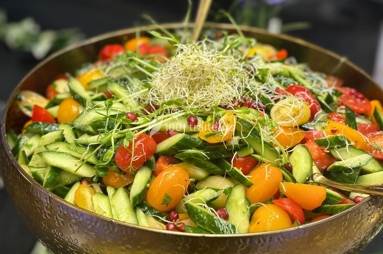 Salade colorée composée de concombres, tomates cerises, graines de grenade et germes, servie dans un grand bol.