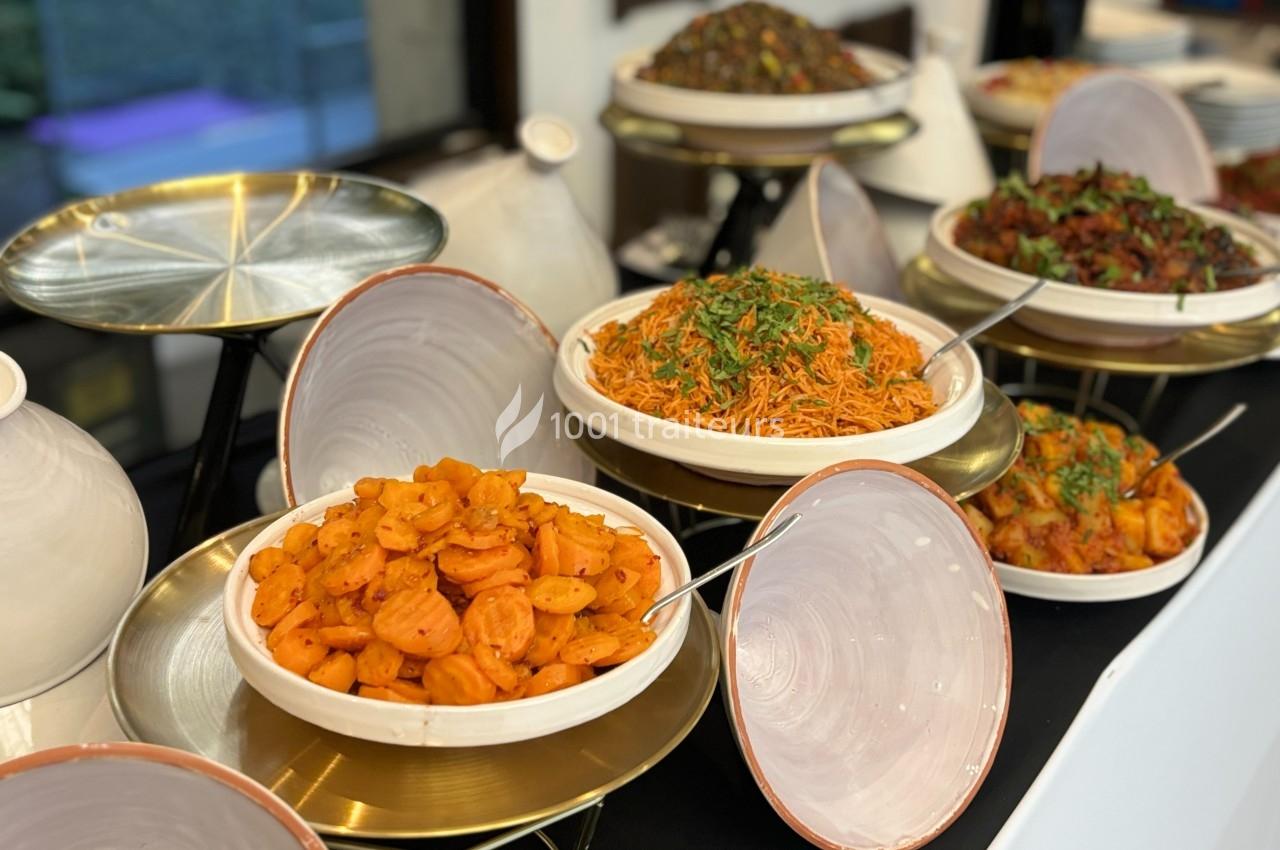 Buffet avec des plats variés, dont des carottes assaisonnées, des nouilles et des légumes sautés, présentés sur des plateaux.