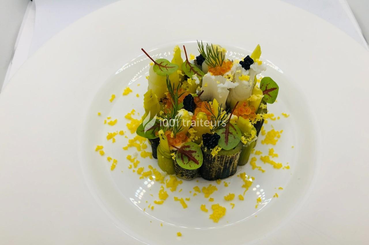 Assiette gastronomique composée de légumes, œufs de poisson, herbes fraîches et zestes jaunes sur une base blanche.