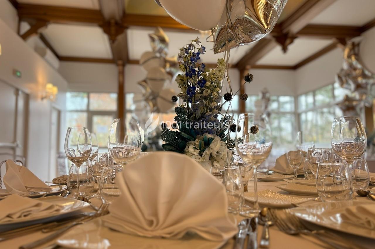 Table élégamment dressée avec serviettes pliées, verres, couverts et centre de table floral bleu et blanc.